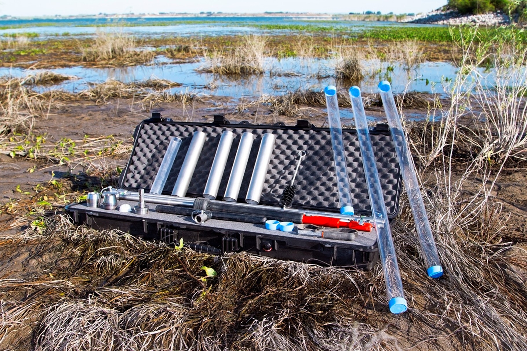 Sludge sampling tools in a case on a wetland landscape, with a pond in the background.