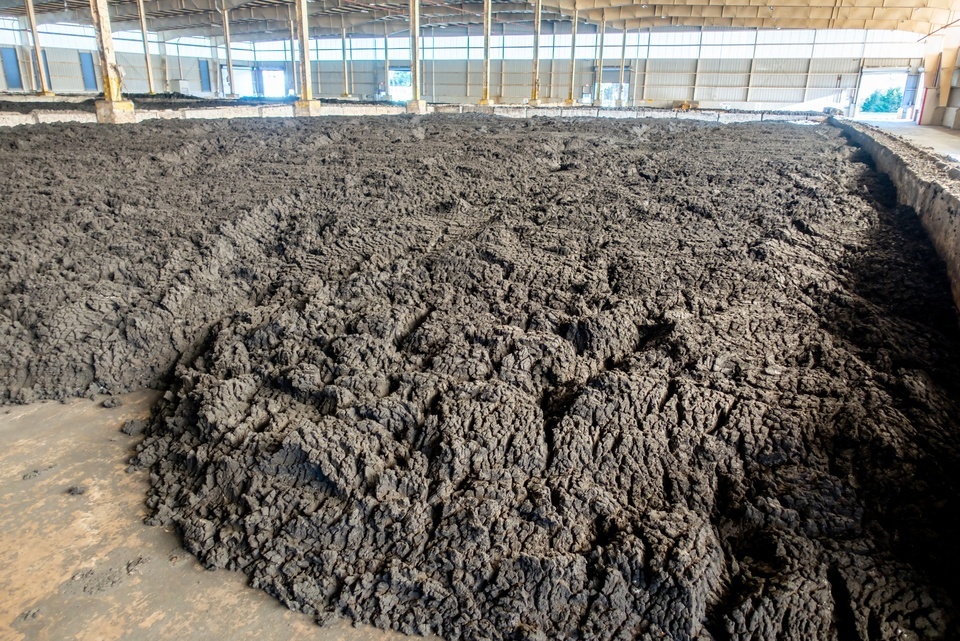 Biosolids sludge sits in a large pile inside a covered storage facility with metal beams and natural lighting.