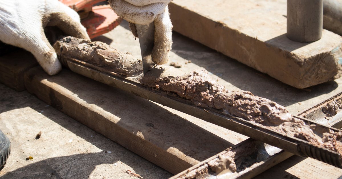 A pair of white-gloved hands scrape wet clay from a split spoon sampler resting on a concrete surface.