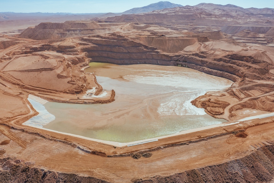 Bubbling, multicolored water fills an active tailings dam surrounded by exposed earth and access roads.