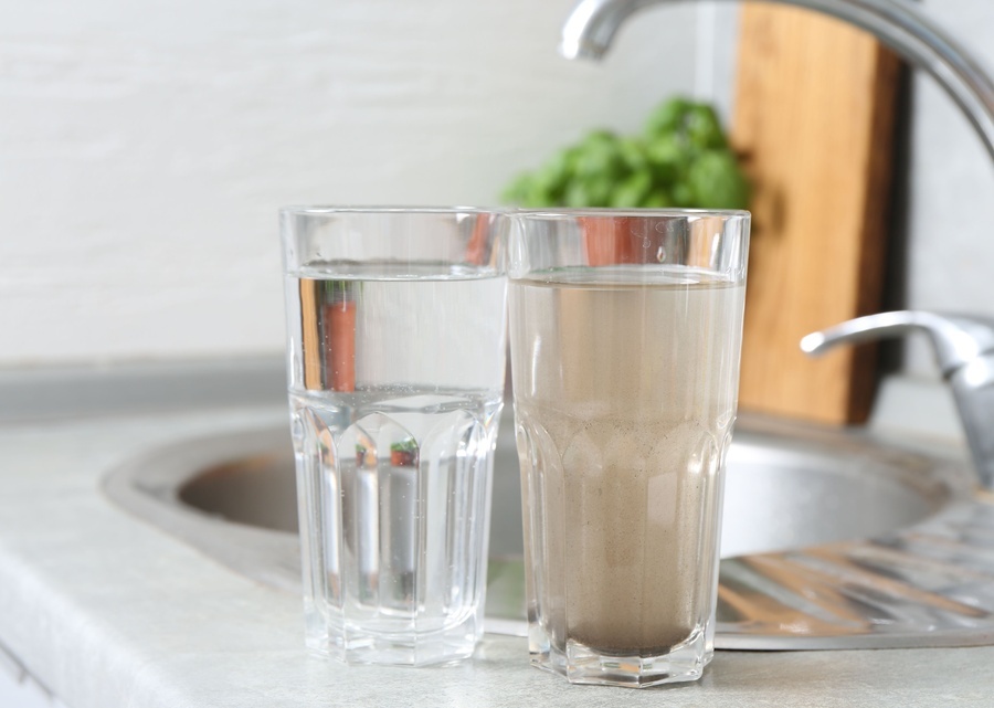 Two glasses full of water rest on a kitchen counter. One glass has clear water and the other has cloudy, brown water.