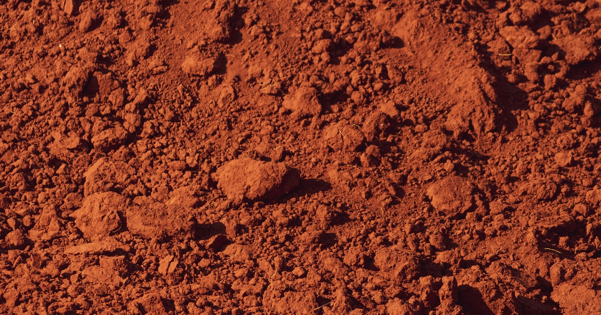 A close-up of reddish-brown soil with a clumpy texture and small to medium-sized dirt clods throughout.