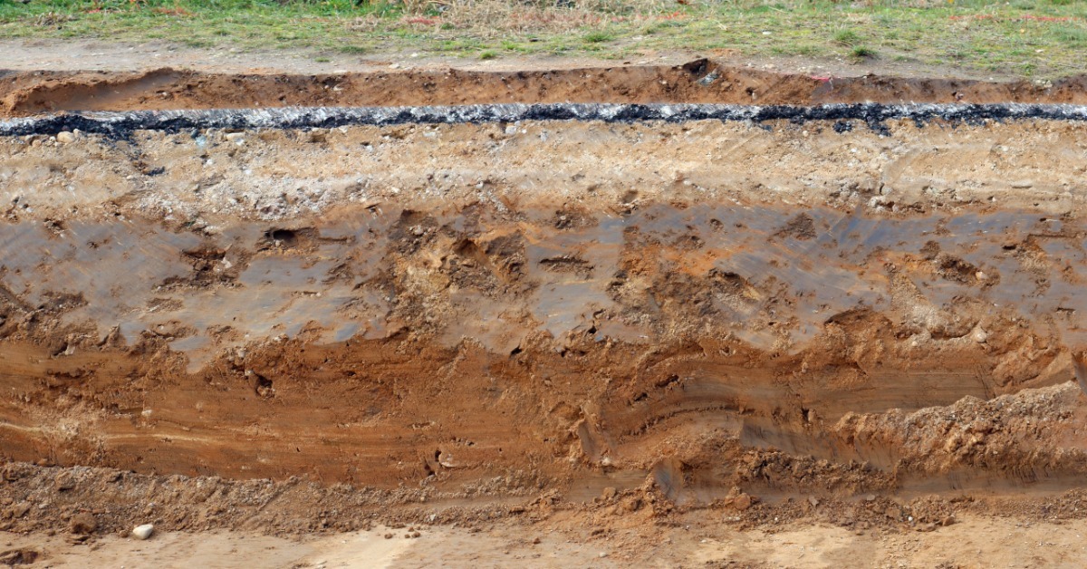 A close-up view shows dry, rocky soil clumps and loose reddish sediment across a rough ground surface in sunlight.
